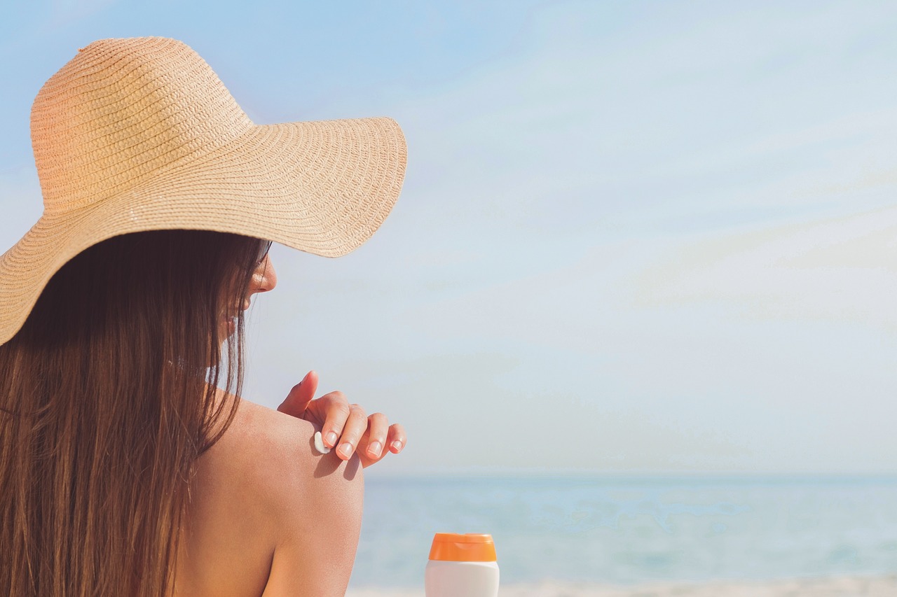 donna con cappello di paglia che si spalma la crema solare sulla pelle